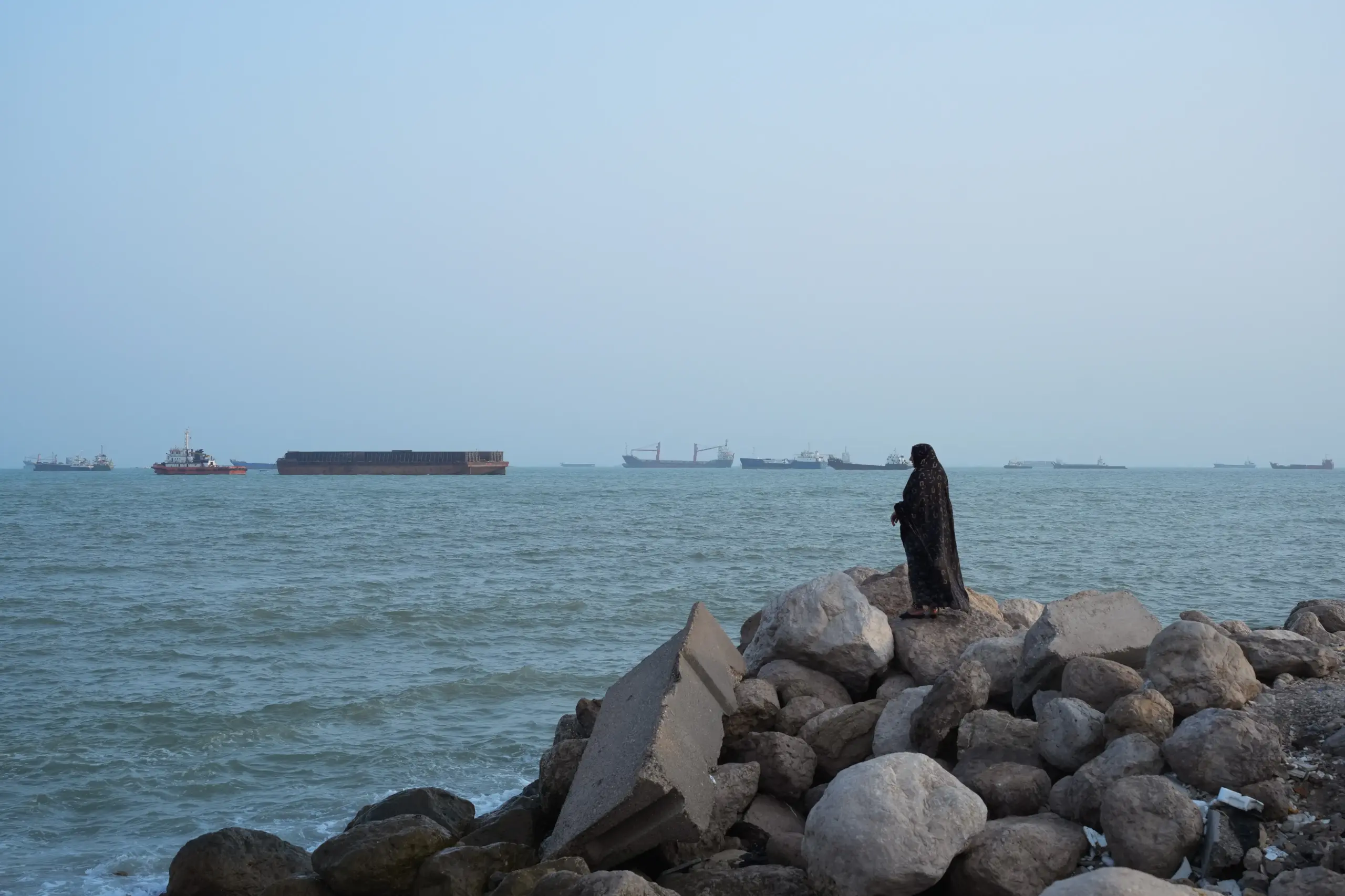 A women stands overlooking the water as ships are seen anchored in the Strait of Hormuz on August 10, 2026, off the coast of Bandar Abbas, Iran.